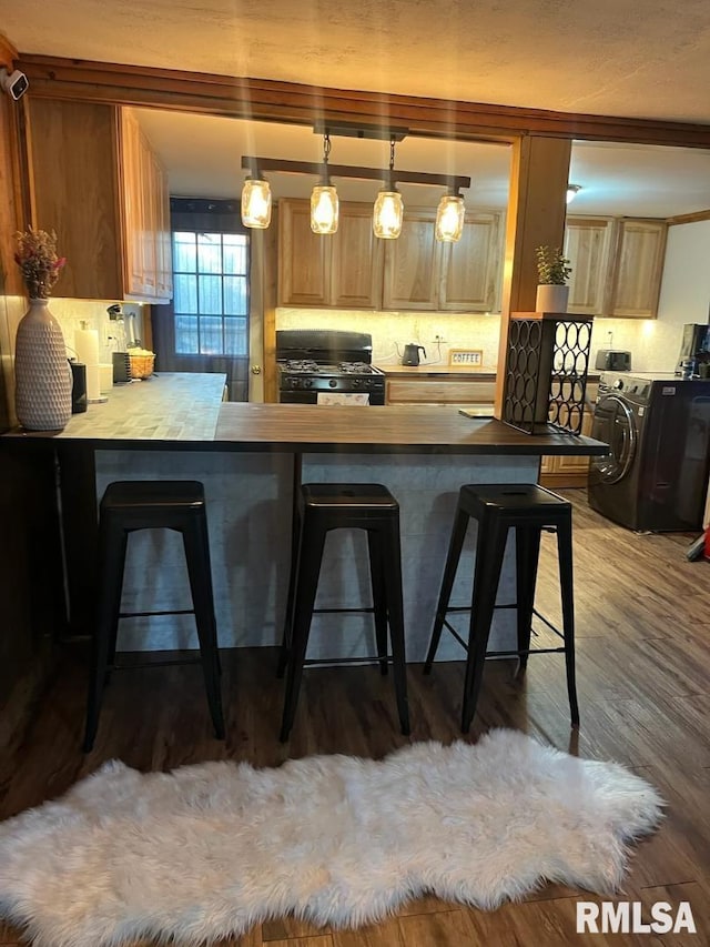 kitchen with hardwood / wood-style flooring, gas stove, a breakfast bar area, kitchen peninsula, and backsplash