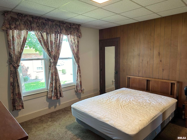 carpeted bedroom featuring a paneled ceiling and wooden walls