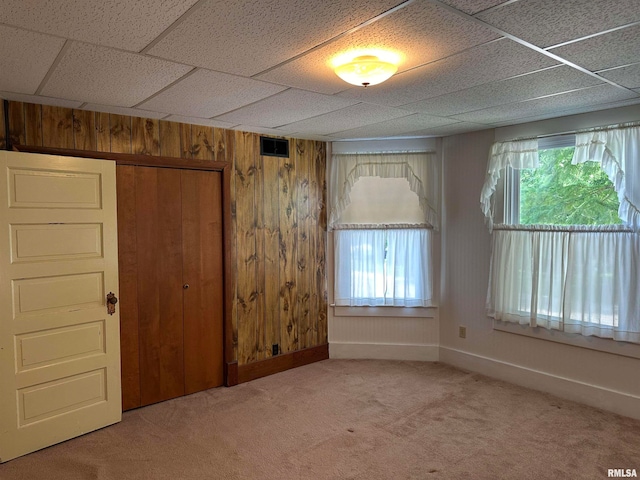 unfurnished bedroom featuring wood walls, a drop ceiling, a closet, and carpet floors