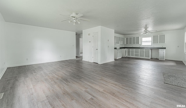 unfurnished living room featuring sink, wood-type flooring, and ceiling fan