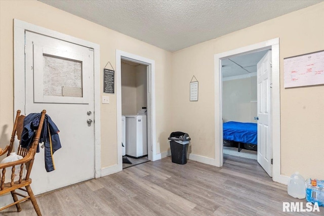 hallway featuring washing machine and clothes dryer, a textured ceiling, and light wood-type flooring