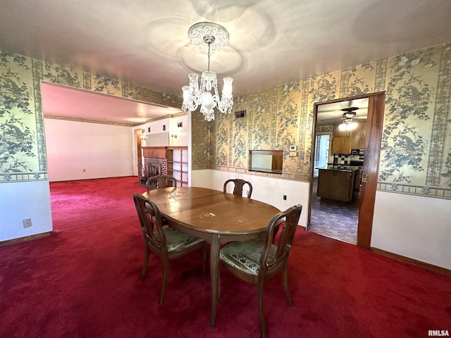 carpeted dining room with wallpapered walls, baseboards, visible vents, a fireplace, and ceiling fan with notable chandelier