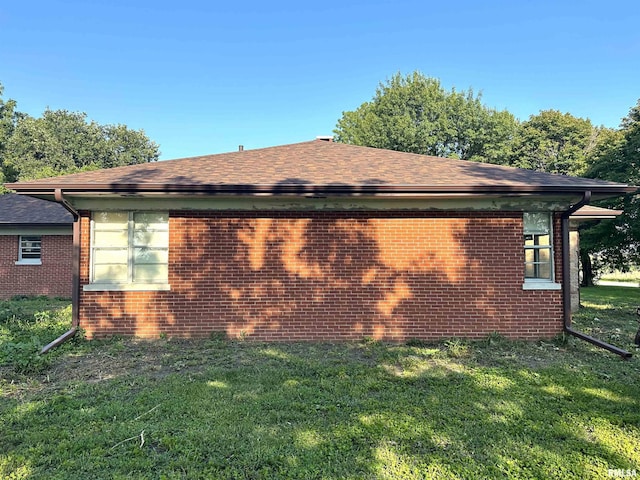 view of side of property featuring brick siding, a yard, and roof with shingles