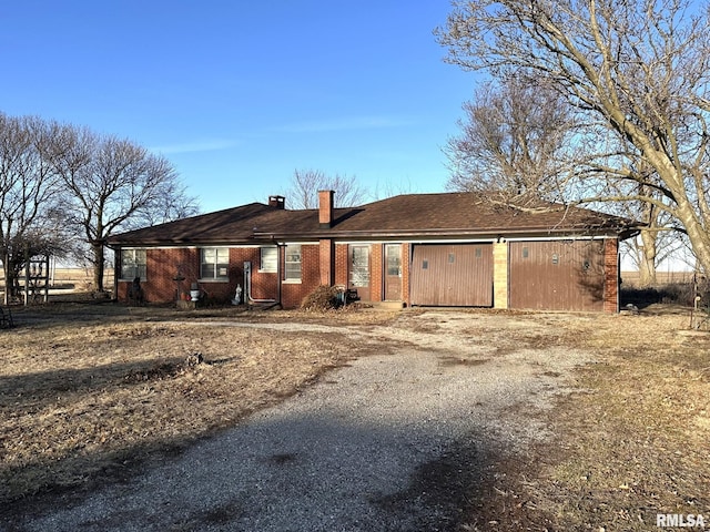 rear view of house featuring brick siding, driveway, a chimney, and an attached garage