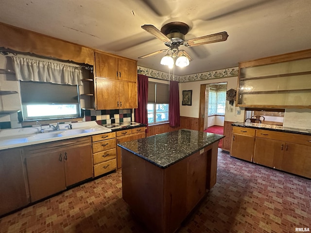 kitchen featuring a wainscoted wall, open shelves, a kitchen island, brown cabinetry, and ceiling fan