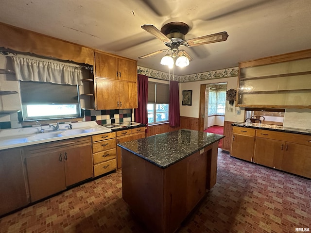 kitchen with a ceiling fan, a wainscoted wall, a kitchen island, brown cabinets, and open shelves