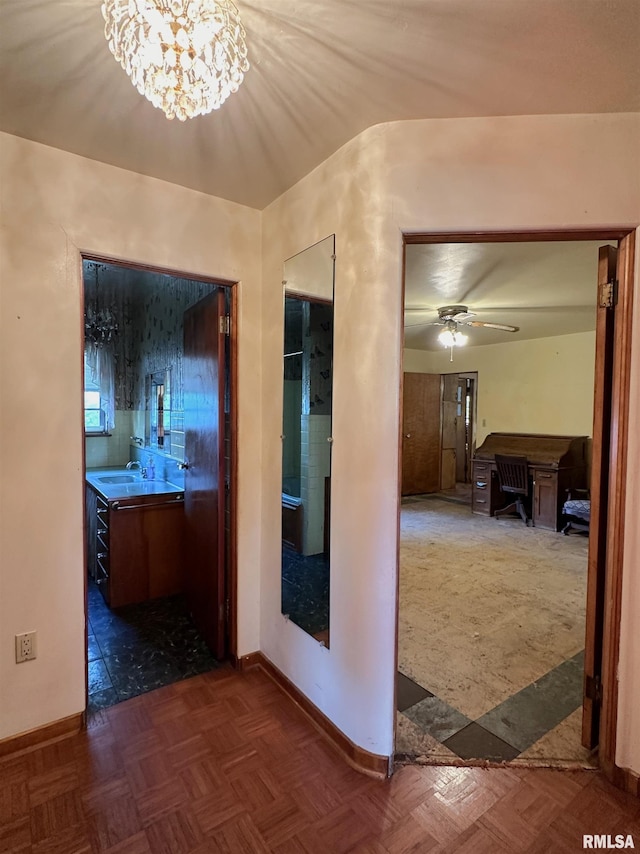 hall featuring an inviting chandelier, a sink, and baseboards