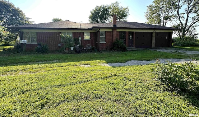 rear view of property with a garage, brick siding, a lawn, and driveway