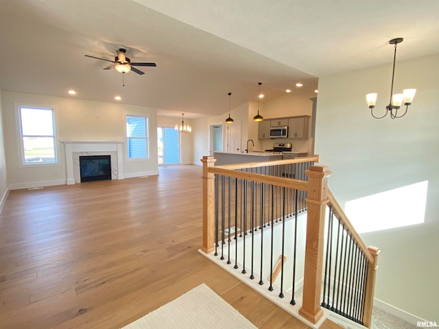 interior space with sink, hardwood / wood-style floors, lofted ceiling, a tiled fireplace, and ceiling fan with notable chandelier