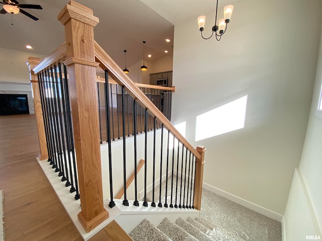 stairs with hardwood / wood-style floors, ceiling fan with notable chandelier, and lofted ceiling