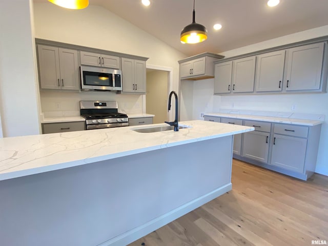 kitchen with hanging light fixtures, sink, vaulted ceiling, light stone countertops, and appliances with stainless steel finishes