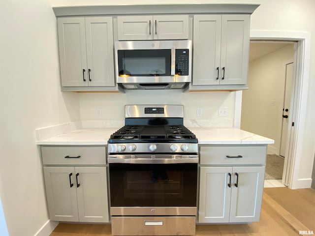 kitchen featuring light stone countertops, appliances with stainless steel finishes, light hardwood / wood-style floors, and gray cabinets