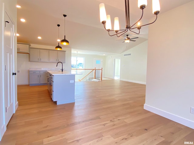 kitchen with light wood-type flooring, vaulted ceiling, a kitchen island with sink, pendant lighting, and gray cabinets