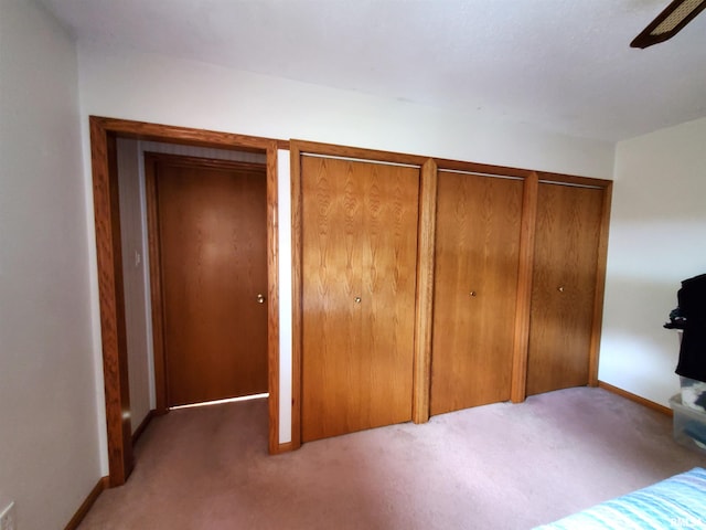 unfurnished bedroom with two closets, ceiling fan, and light colored carpet