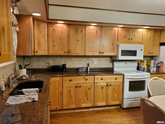 kitchen with hardwood / wood-style flooring, sink, backsplash, white appliances, and dark stone countertops