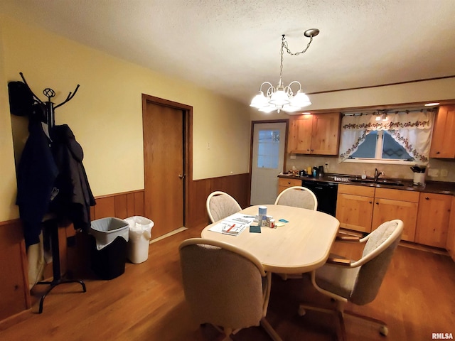 dining room featuring dark wood-type flooring, wood walls, a textured ceiling, sink, and a chandelier