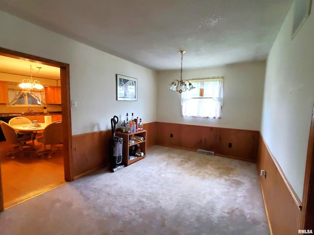 carpeted empty room featuring wood walls and a chandelier