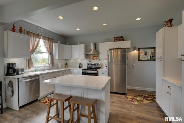 kitchen with appliances with stainless steel finishes, backsplash, light hardwood / wood-style flooring, wall chimney range hood, and a kitchen island