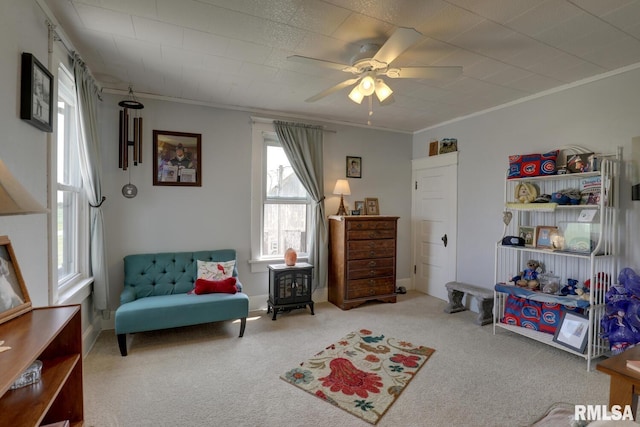 living area featuring a wood stove, ornamental molding, carpet flooring, and ceiling fan