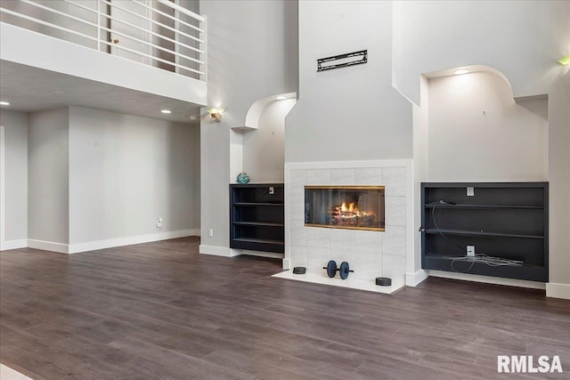 unfurnished living room featuring hardwood / wood-style flooring, a towering ceiling, and a tile fireplace