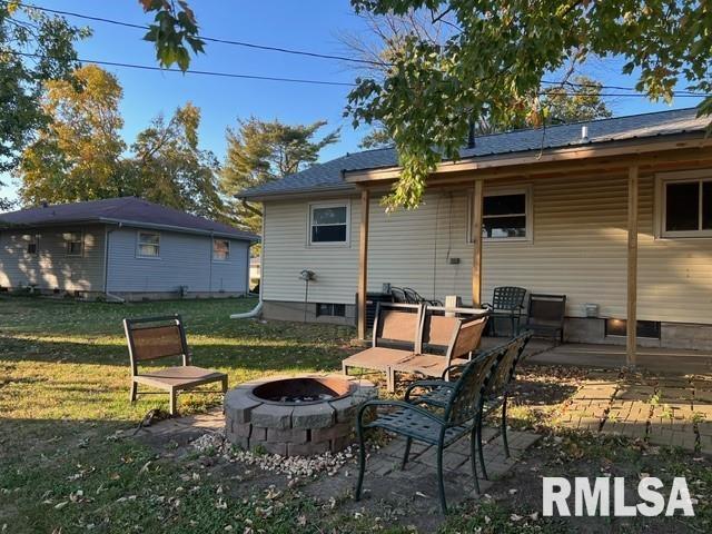 rear view of property featuring a yard, a patio, and an outdoor fire pit