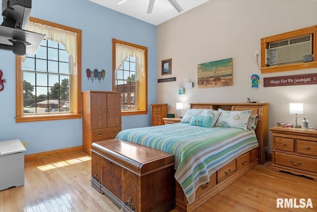 bedroom with a wall mounted air conditioner, light wood-type flooring, multiple windows, and ceiling fan