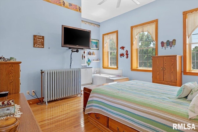 bedroom featuring multiple windows, light wood-type flooring, radiator, and ceiling fan