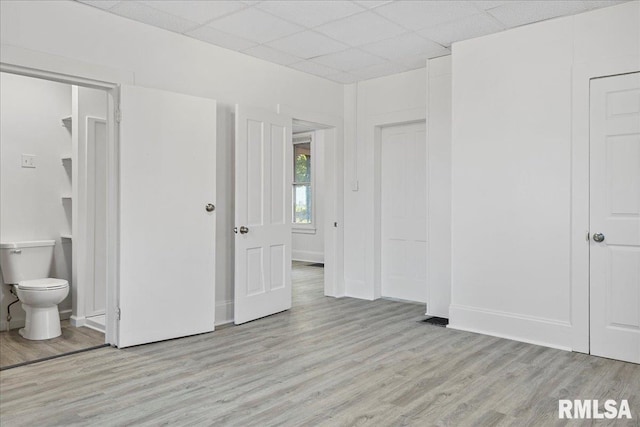 unfurnished bedroom with light hardwood / wood-style flooring, ensuite bathroom, and a drop ceiling