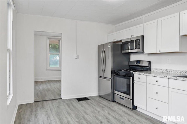 kitchen with light stone countertops, appliances with stainless steel finishes, white cabinets, and light hardwood / wood-style floors