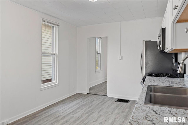 kitchen with light wood-type flooring, white cabinetry, and a healthy amount of sunlight