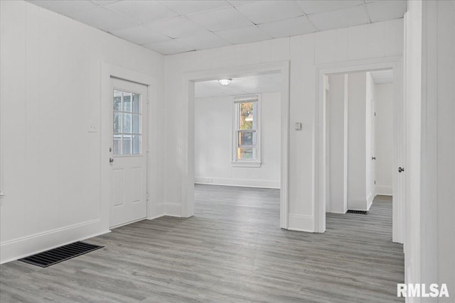 empty room with light wood-type flooring, a wealth of natural light, and a paneled ceiling