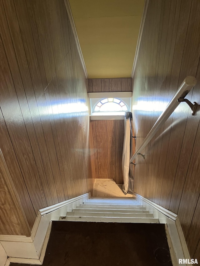 staircase with crown molding and wood walls