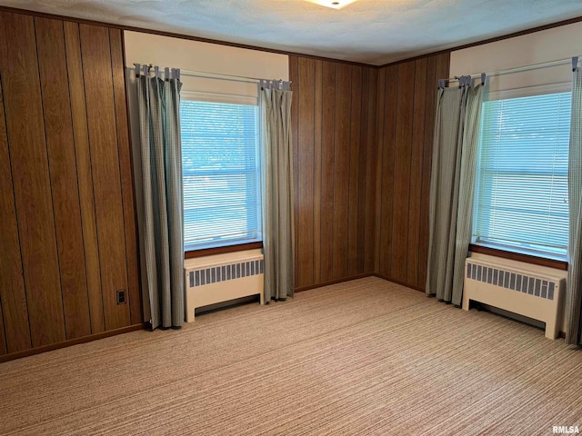 carpeted empty room with wooden walls, radiator, and a textured ceiling