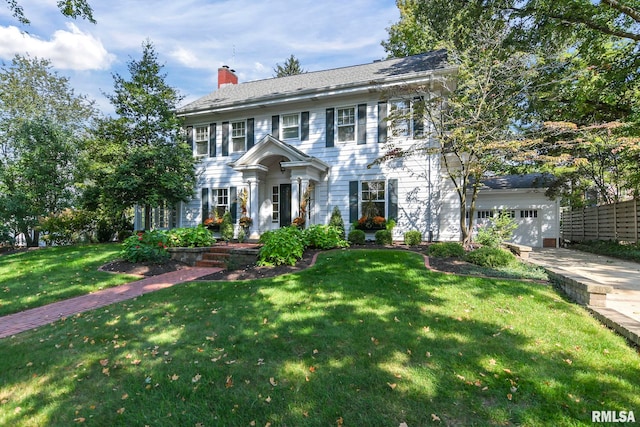 colonial house with driveway, a chimney, and a front yard