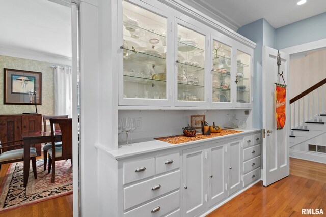 bar featuring crown molding, light wood-type flooring, and white cabinets