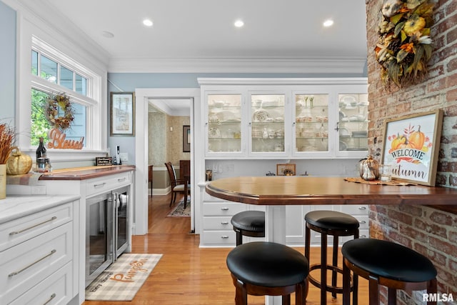 bar featuring light stone counters, light hardwood / wood-style floors, white cabinetry, and ornamental molding