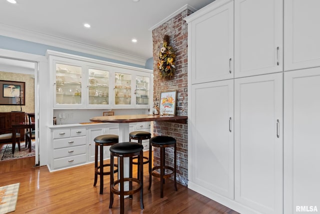 bar with recessed lighting, light wood-style flooring, crown molding, and bar area