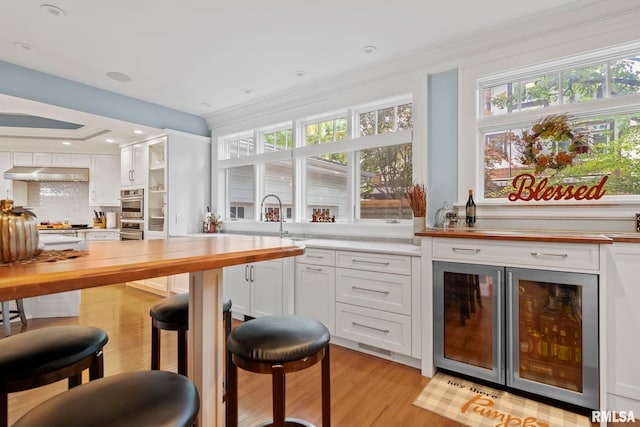 bar with backsplash, light hardwood / wood-style floors, sink, butcher block counters, and white cabinets