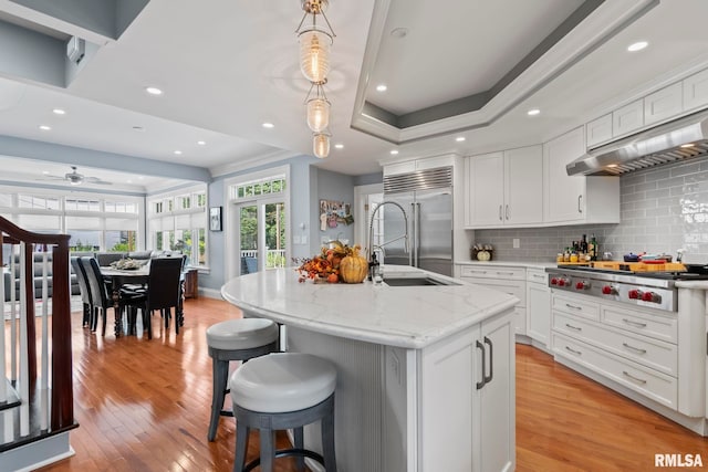 kitchen with decorative light fixtures, appliances with stainless steel finishes, light stone counters, light hardwood / wood-style floors, and an island with sink