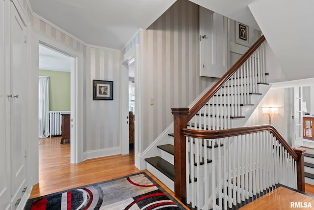 staircase with baseboards, wood finished floors, and wallpapered walls