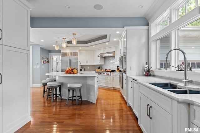 kitchen with stainless steel built in refrigerator, a kitchen island with sink, sink, hardwood / wood-style flooring, and white cabinets