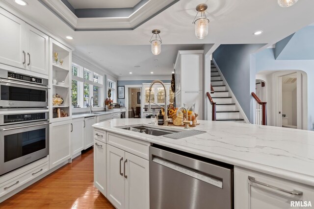 kitchen with crown molding, decorative light fixtures, light wood-type flooring, light stone countertops, and stainless steel appliances