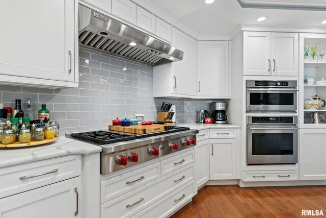 kitchen featuring ventilation hood, light hardwood / wood-style flooring, appliances with stainless steel finishes, and white cabinets