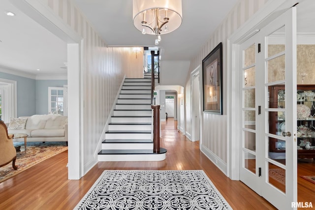 stairway featuring hardwood / wood-style floors, a wealth of natural light, a notable chandelier, and ornamental molding