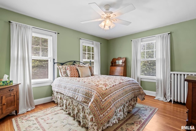 bedroom with ceiling fan, radiator, light wood-type flooring, and baseboards