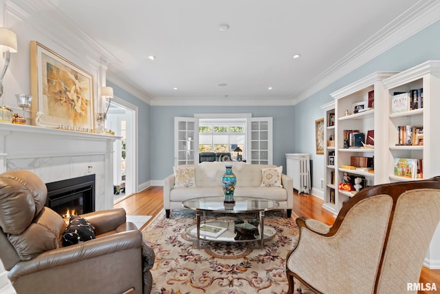 living room with a tiled fireplace, radiator heating unit, wood finished floors, and ornamental molding