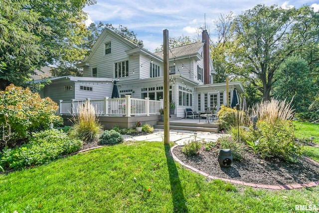 back of property featuring a lawn, a chimney, and a wooden deck