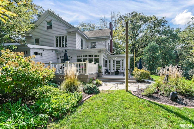 back of house featuring a wooden deck, a lawn, a chimney, and a sunroom