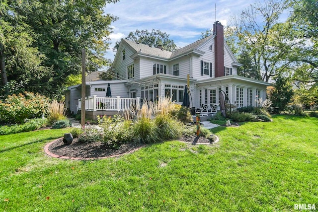 back of property featuring a lawn, a chimney, a deck, and a sunroom