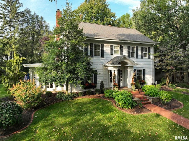 colonial-style house with roof with shingles, a chimney, and a front yard